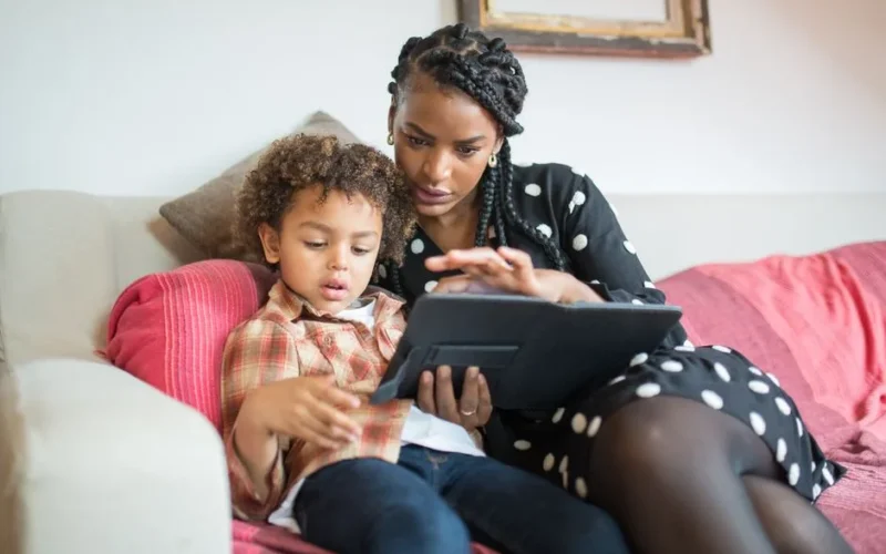 A caring mother and her son using a tablet together on a cozy couch at home.