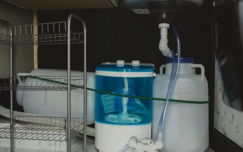 Compact travel-size washer in a storage area with plastic containers and tubing system.