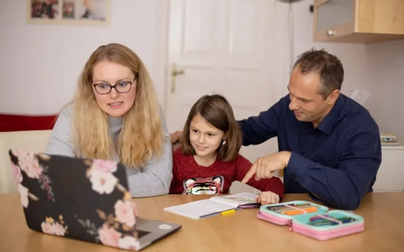 A family is engaged in homeschooling, using technology to learn together in a cozy home setting.