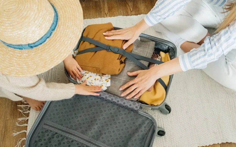 A woman and child pack clothes in a suitcase, preparing for a vacation.