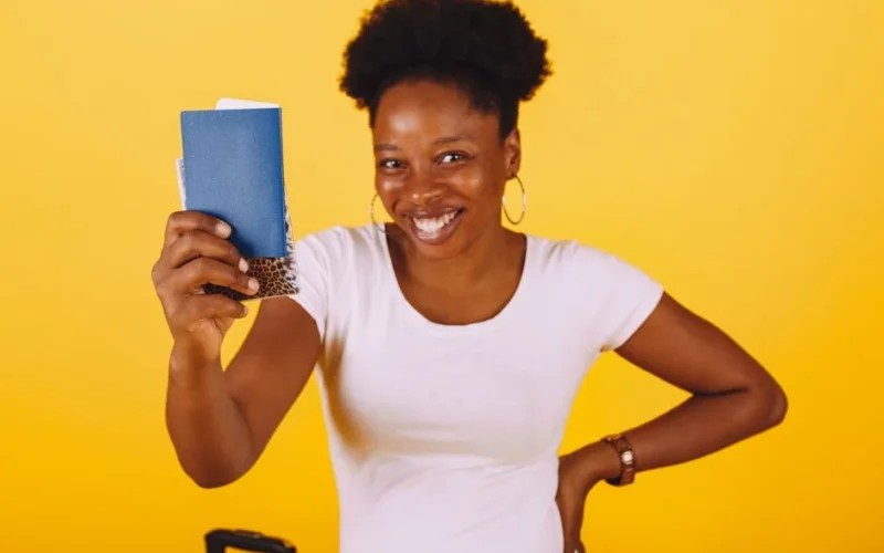 Smiling woman holding a passport, ready for a travel adventure against a yellow background.