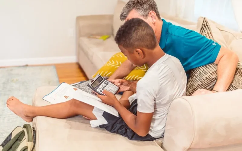 A father and son engaged in learning with a calculator on a cozy living room couch.