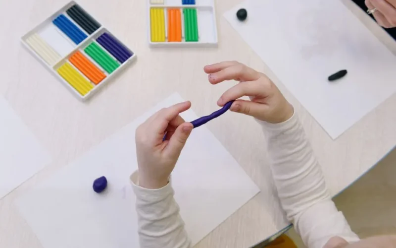 Overhead view of a child shaping purple modelling clay, surrounded by colorful clay sticks.