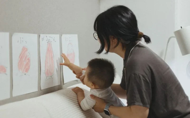 A mother and child engage in a learning activity, exploring art drawings in a cozy indoor setting.