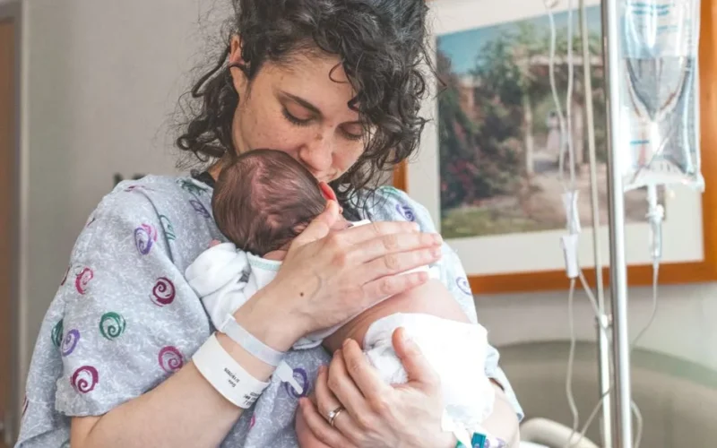 Mother gently holding newborn baby in hospital setting, showcasing warmth and love.