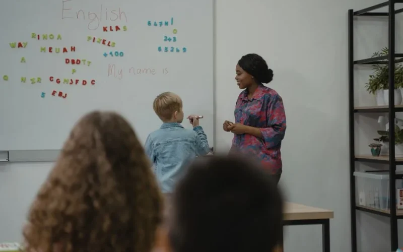 A teacher engages students in an interactive English lesson using a whiteboard and magnetic letters.