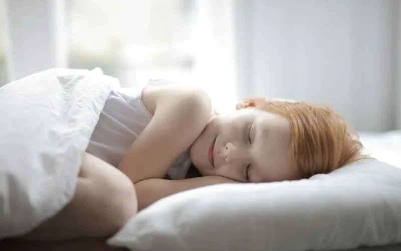 A young girl peacefully sleeping in a bright bedroom, conveying comfort and relaxation.