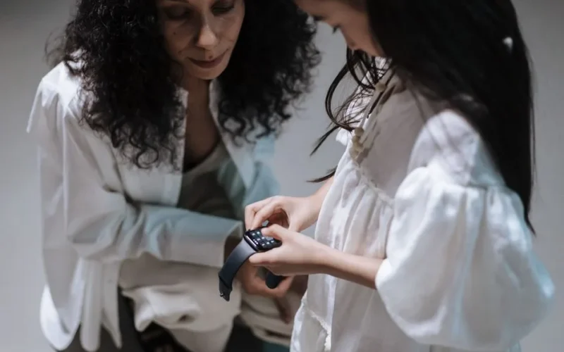 A mother and daughter interact with a smartwatch, showcasing family bonding with modern tech.