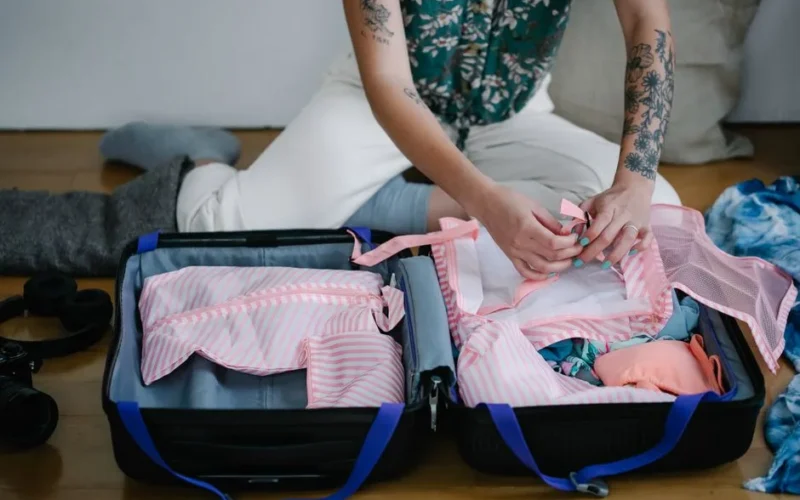 A woman packing her travel suitcase on the floor indoors, preparing for a trip.