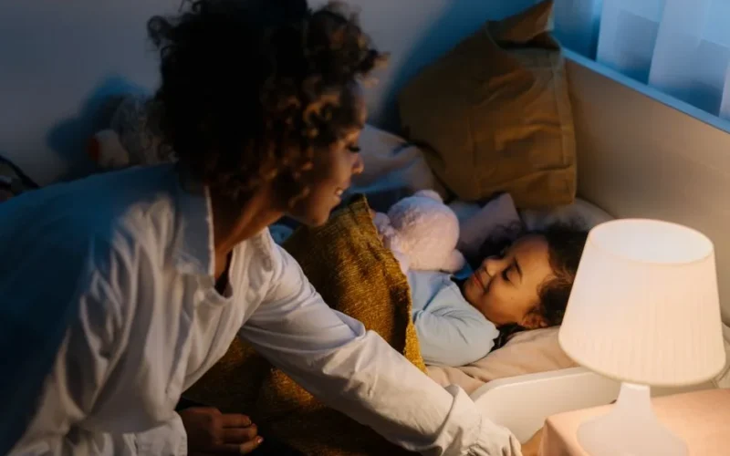A warm moment of a mother tucking her young daughter into bed under a cozy blanket.