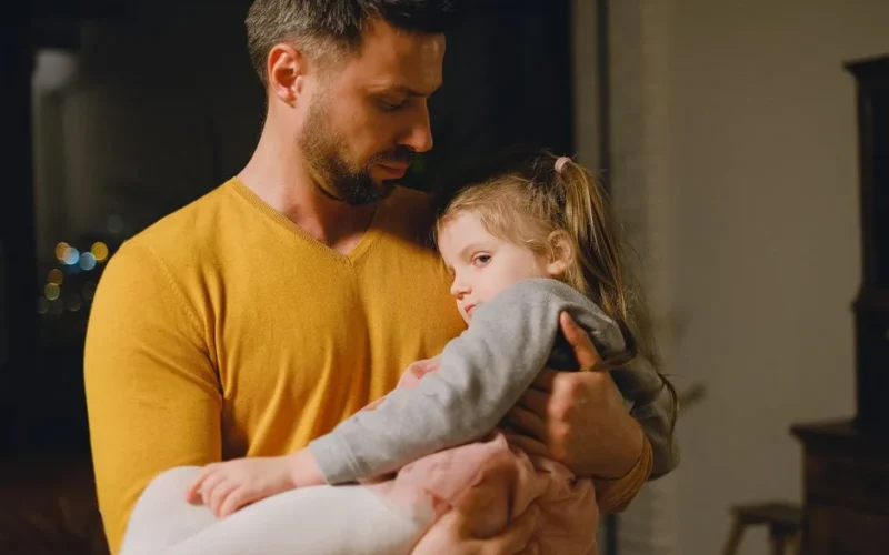 A father gently cradling his young daughter, showcasing affection and family bonding.