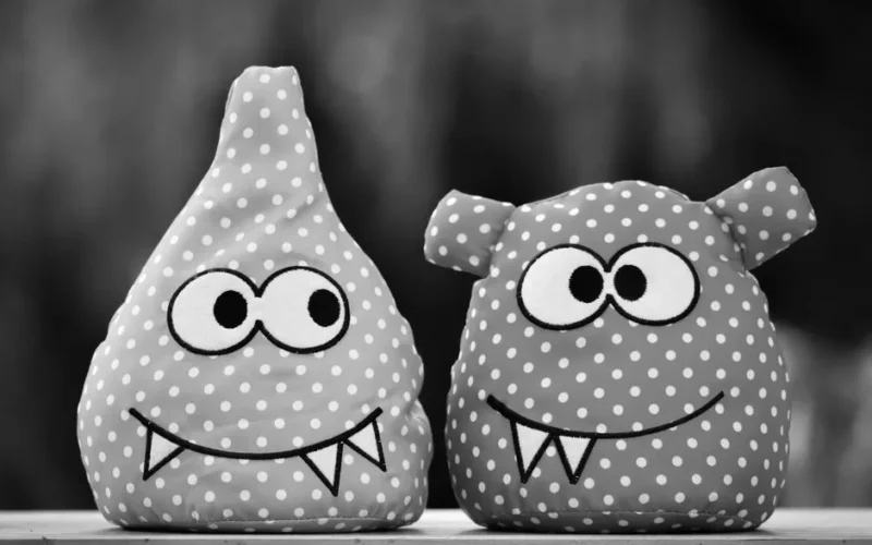 Two adorable polka dot plush monster toys with big eyes and fangs on a wooden surface.