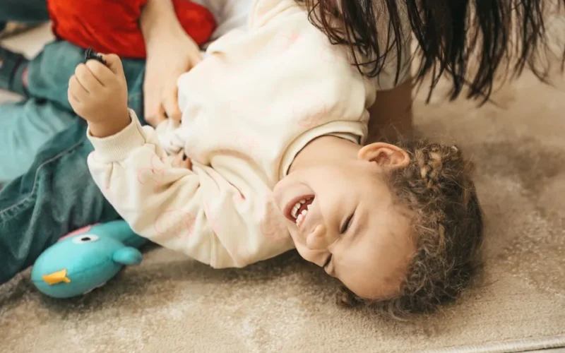 A happy child laughs while playing with a parent indoors, capturing pure joy and innocence.