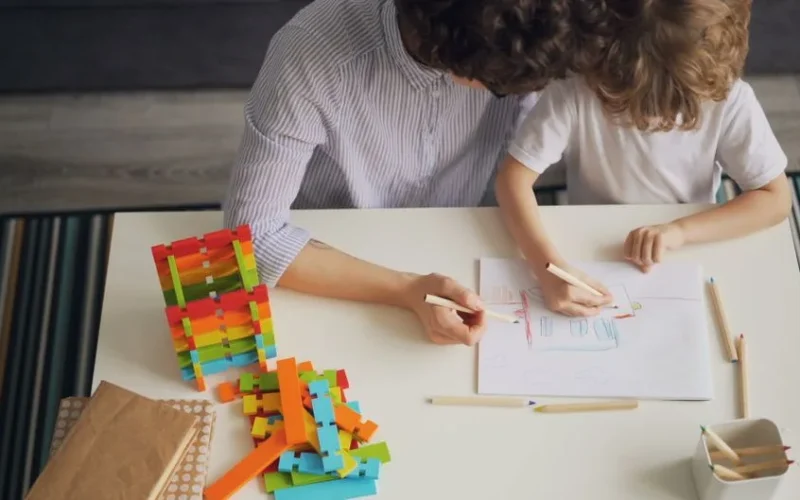 A mother and child drawing with colored pencils at a table, fostering creativity and learning.