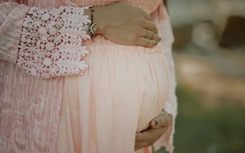 Close-up of a pregnant woman embracing her belly in a delicate pink dress.