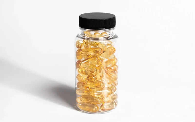 Close-up of a transparent bottle filled with yellow softgel capsules in a minimalist style.