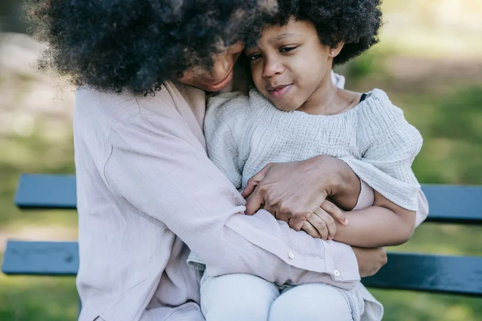 Tender moment between a mother and daughter embracing on a park bench.