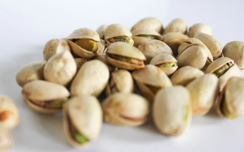 A close-up of fresh pistachio nuts scattered on a white surface, showcasing their natural shells and vibrant color.