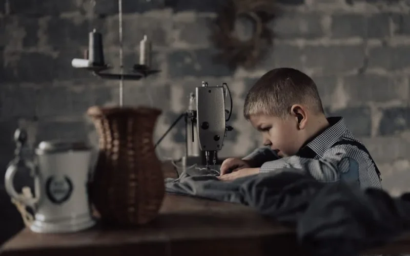 A young boy intently sewing with a machine in a workshop setting, showcasing concentration and skill.