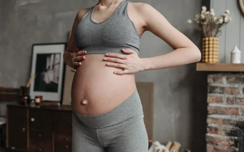 Pregnant woman in activewear enjoys wellness indoors, holding baby bump in a cozy setting.