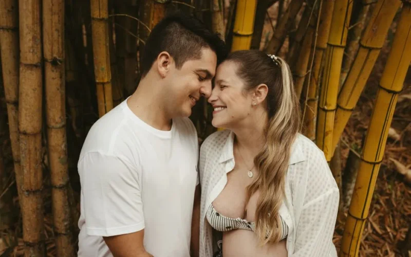 Happy couple embracing in a lush bamboo forest, celebrating pregnancy and love.