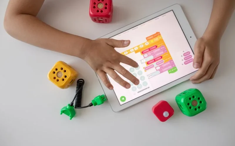 Child using digital tablet for coding education alongside colorful toy blocks.