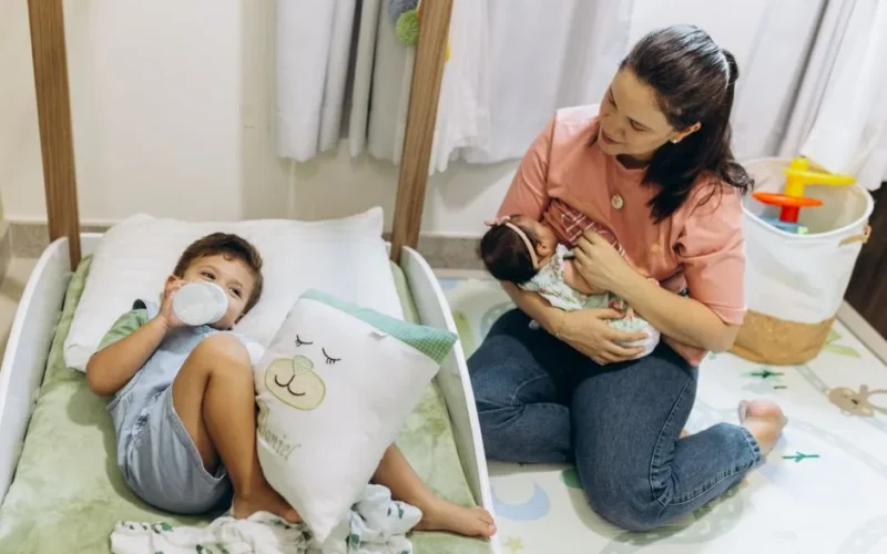Mother with baby and young child in a warm, nurturing nursery environment.