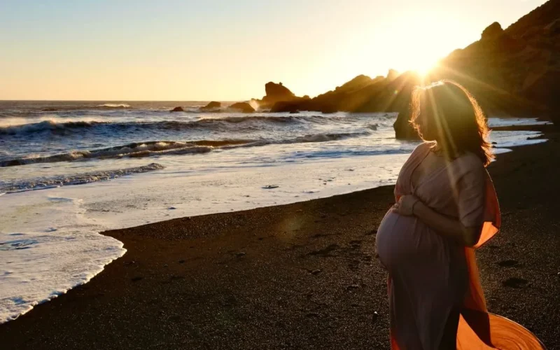 Expectant woman standing on Vík Beach, Iceland at sunset, embracing motherhood.