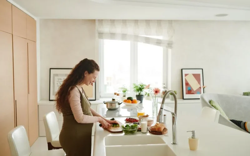 Pregnant woman slicing vegetables in a bright kitchen setting, embracing healthy lifestyle.