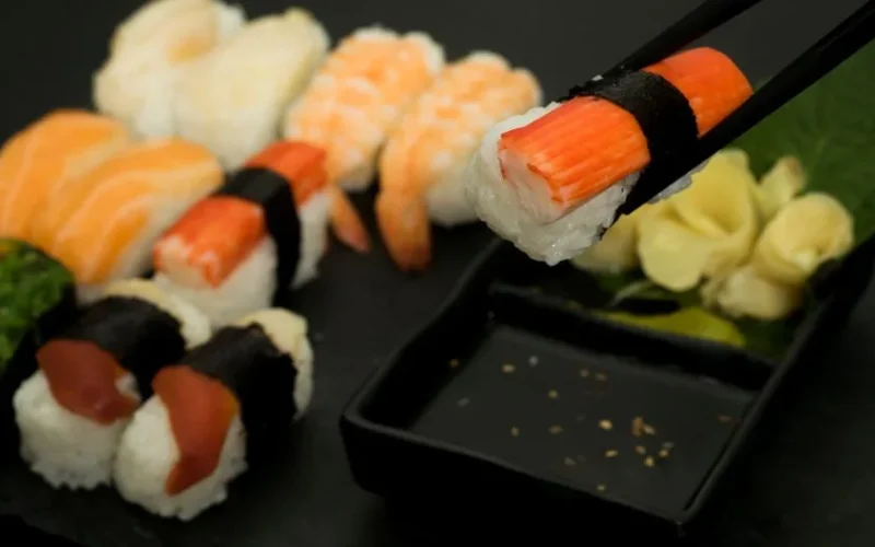 Vibrant sushi pieces with chopsticks highlighting fresh seafood on a black plate.