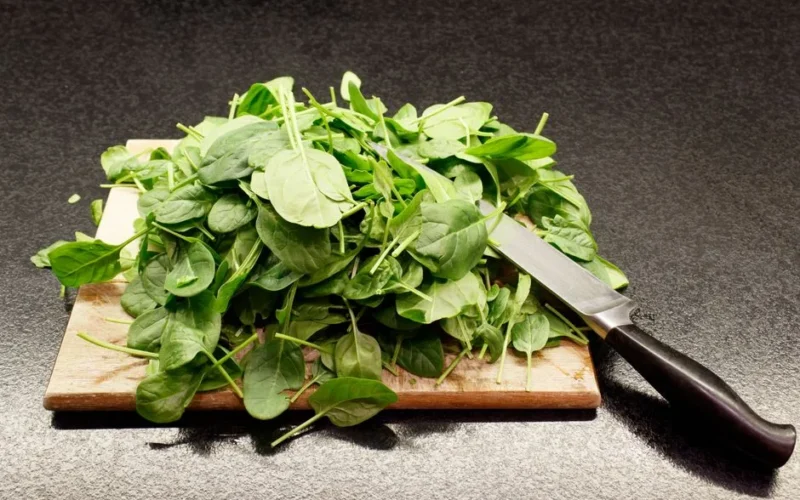 A pile of fresh spinach leaves on a wooden cutting board with a knife nearby.