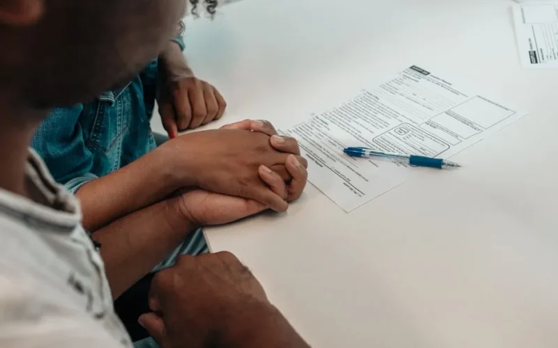 A family supports each other during an adoption process, holding hands over important documents.