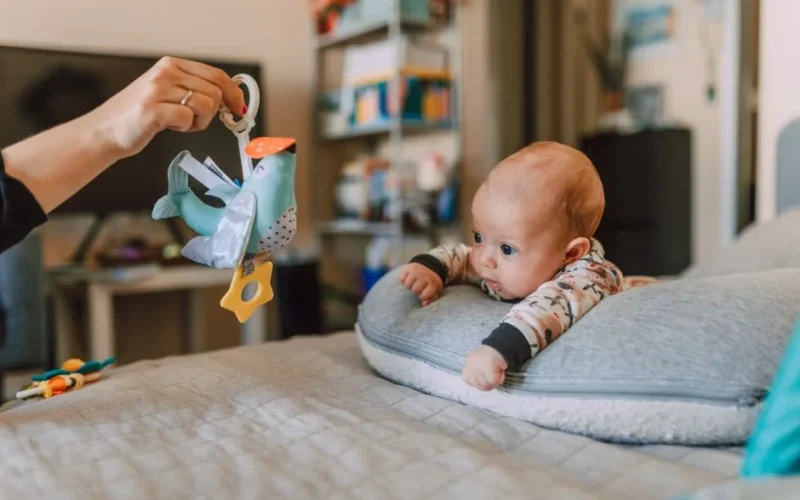 Cute baby showing curiosity while playing with a colorful bird toy in a cozy indoor setting.