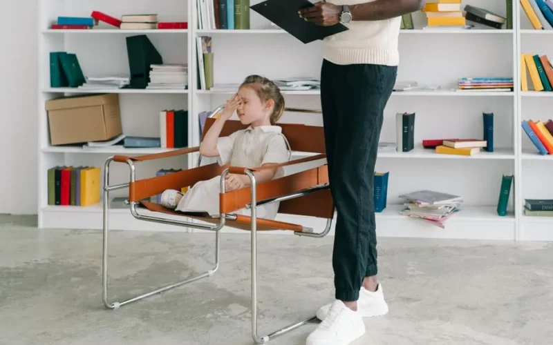 A child in a therapy session with a therapist holding a clipboard.