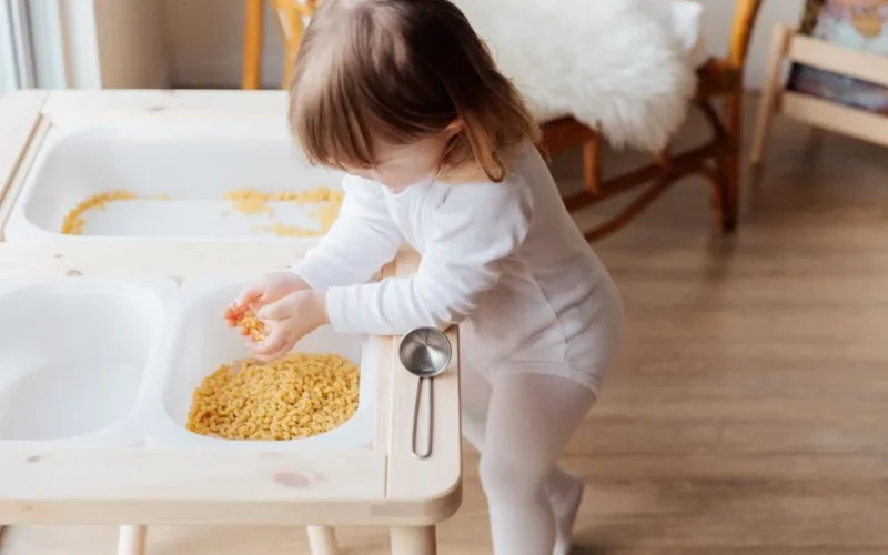 A young child playing with dry pasta in an indoor setting, exploring textures.