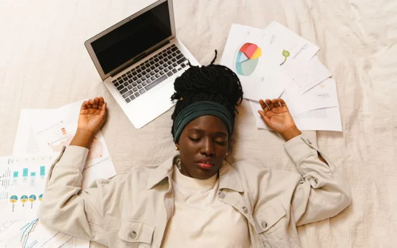 Tired woman with closed eyes lying by laptop and papers after work.