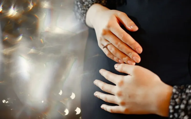 Close-up of a pregnant woman's hands gently resting on her belly, capturing a serene moment.
