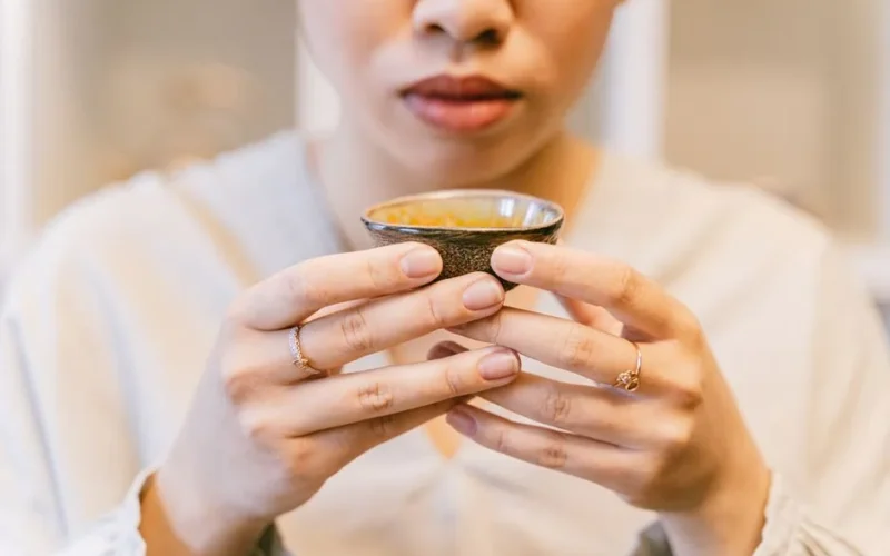 Young woman savoring tea from a ceramic cup indoors. Close-up view.