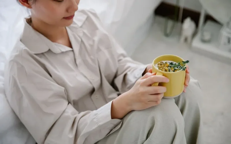 Woman enjoying a hot herbal tea indoors, dressed in cozy sleepwear, promoting relaxation and calm.